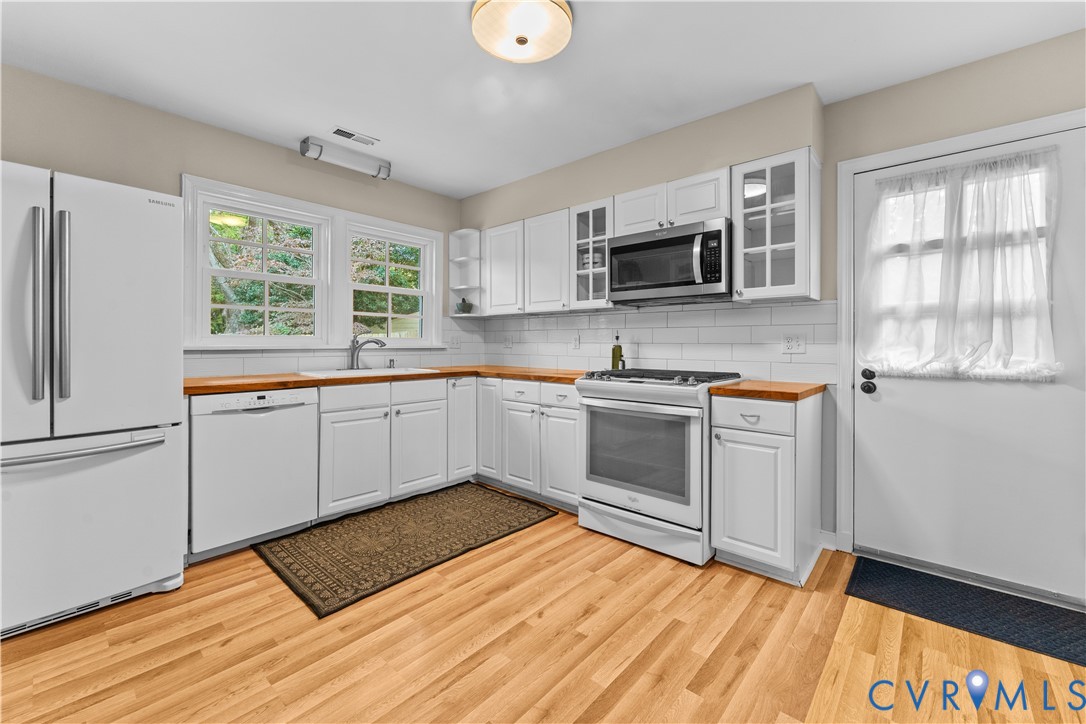 Kitchen featuring white shaker-style cabinetry, butcher block countertops, subway tile backsplash, white appliances, and wood-finish flooring