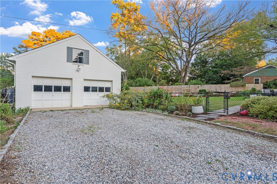Detached two-car garage featuring painted masonry siding, a gravel driveway, and a gated chain-link fence enclosing a backyard area