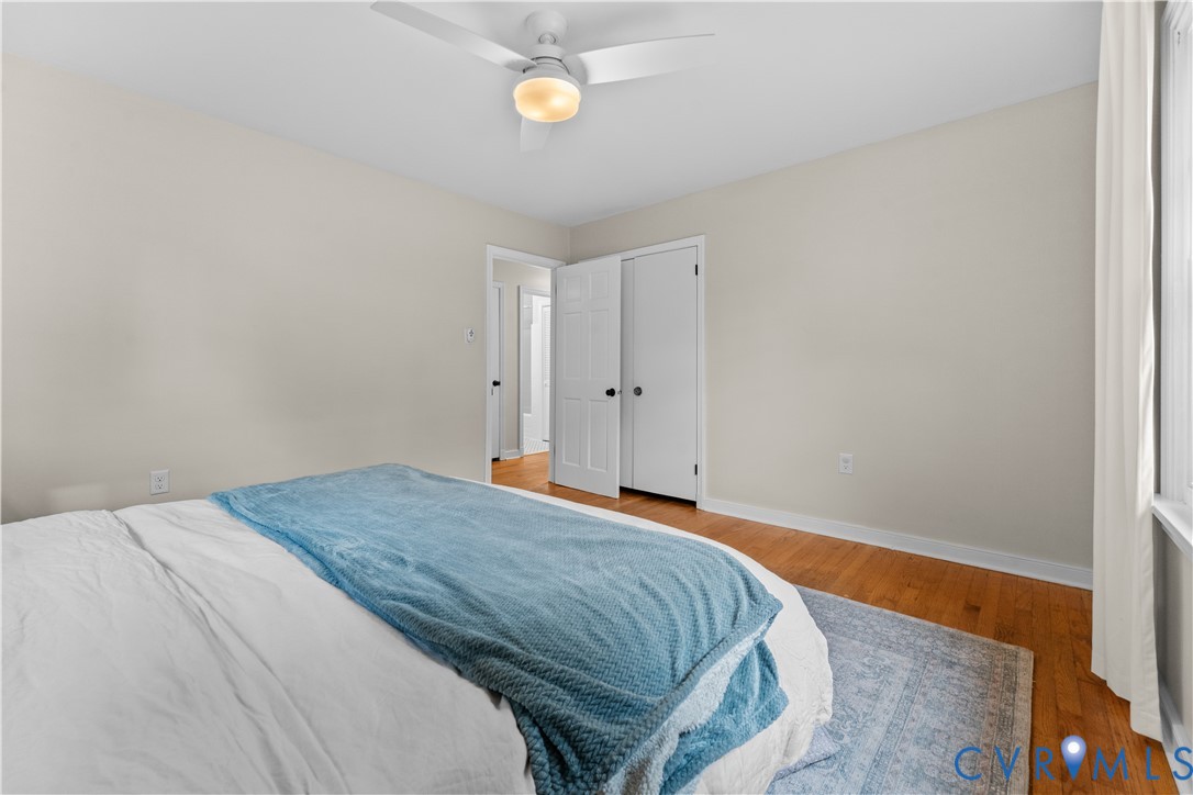 Bedroom featuring wood-finish flooring, a white ceiling fan with integrated lighting, and a double-door closet with six-panel doors