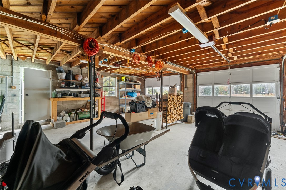 Garage space featuring exposed timber ceiling joists, concrete flooring, concrete block walls, and multi-panel overhead garage doors with rectangular glass panes