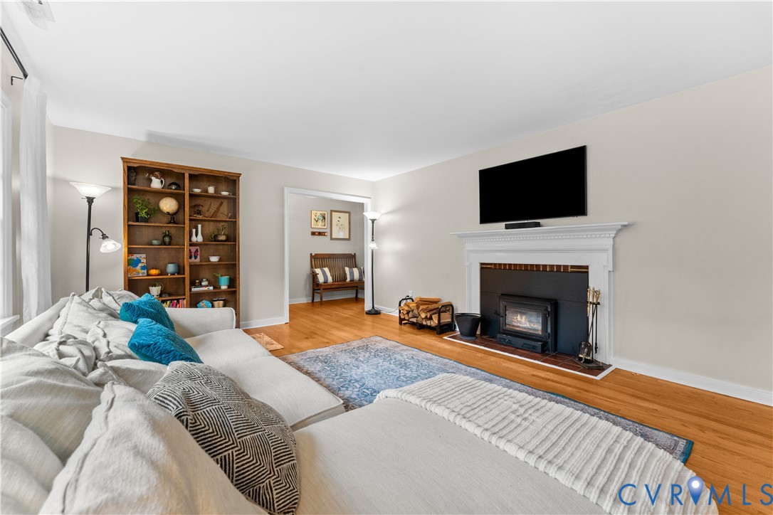 Living area featuring wood-finish flooring, a built-in wooden bookshelf, and a white mantel fireplace with a black insert