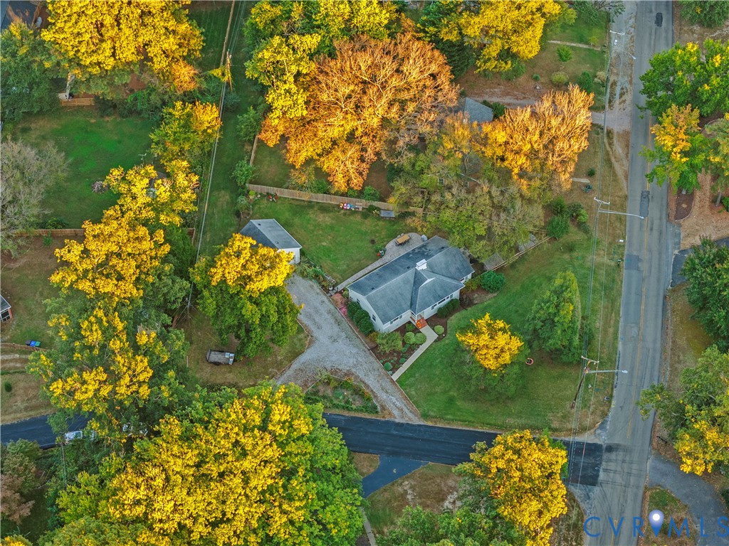 Aerial perspective of a detached residence featuring a multi-gabled roof, an expansive lot with mature tree canopy, a detached garage, and a winding driveway