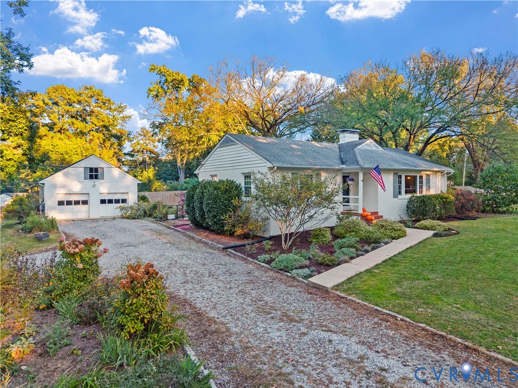 Single-story residence featuring light-colored siding, a detached two-car garage, an expansive gravel driveway, and mature landscaping Single-story residence featuring light-colored siding, a detached two-car garage, an expansive gravel driveway, and mature landscaping