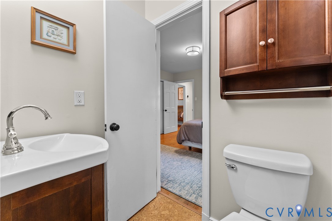 Wall-mounted wooden cabinet with a towel bar, ceramic pedestal sink, polished chrome faucet, and standard toilet
