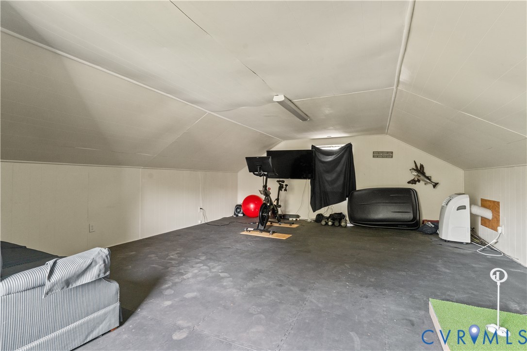Attic space featuring vaulted ceilings, panelled walls, and flooring composed of interlocking foam tiles