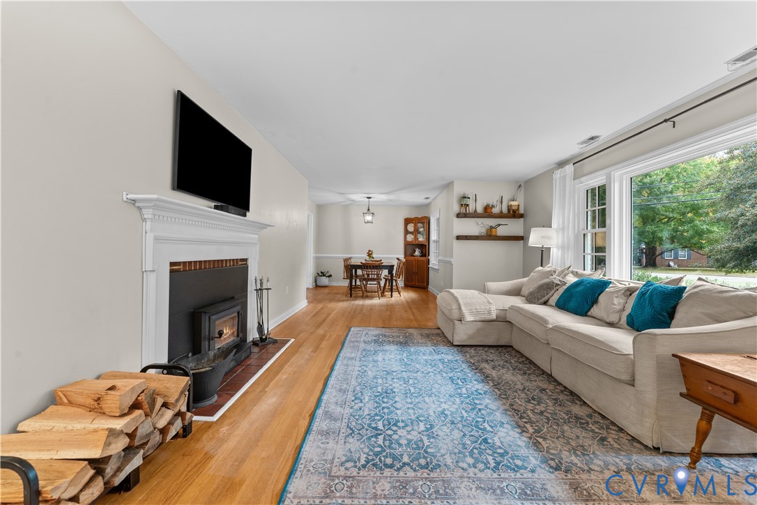 Living area featuring wood-finish flooring, a fireplace with a white mantel, built-in wooden wall shelving, and a large picture window