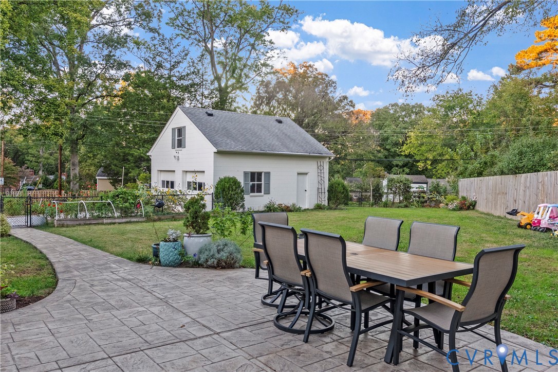 Backyard featuring a stamped concrete patio, manicured lawn, raised garden beds, and a detached two-car garage with white siding