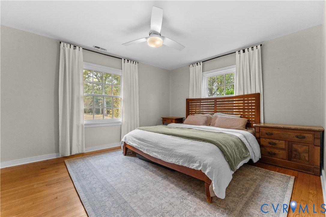 Wood-finish flooring, white multi-pane windows, and a ceiling-mounted light fixture with fan