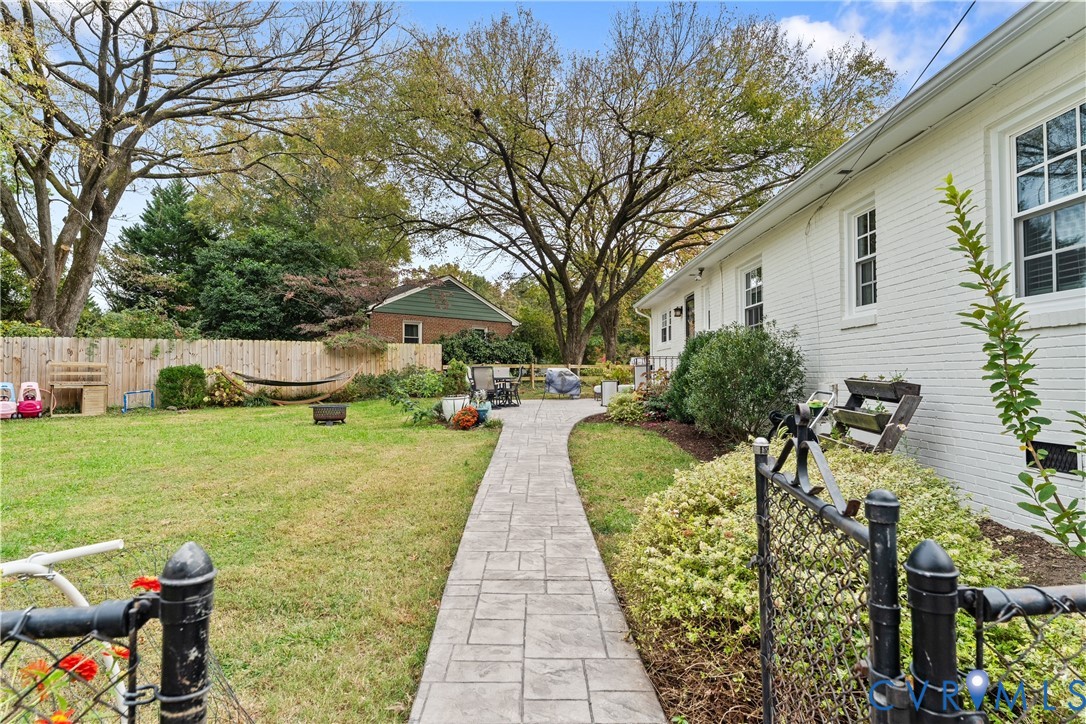 Spacious backyard featuring a stamped concrete walkway, painted brick exterior, wooden privacy fencing, and mature trees