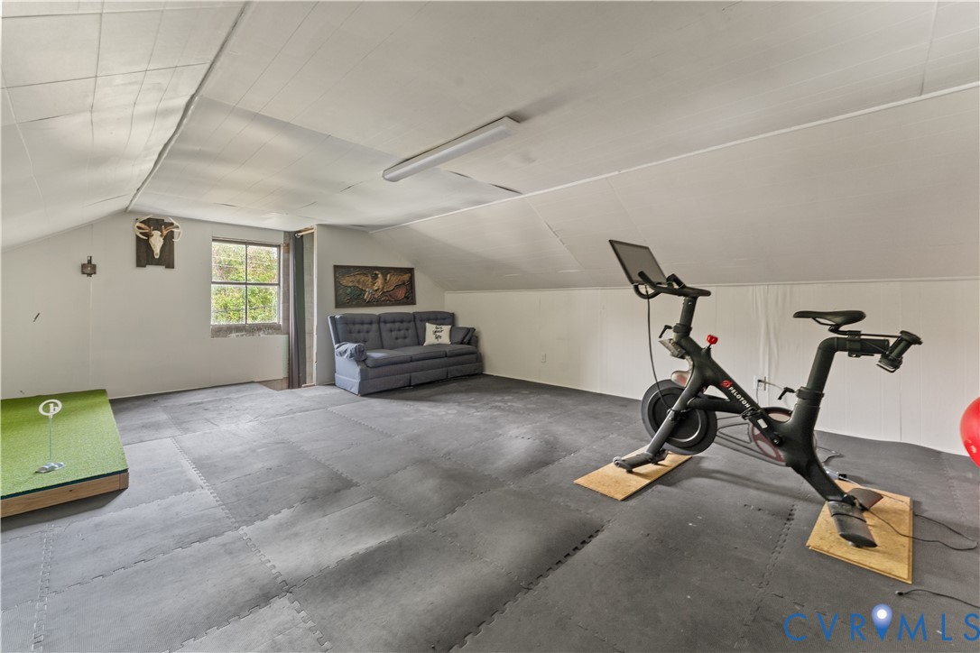 Finished attic space featuring vaulted ceilings, neutral wall finishes, and a window providing natural light