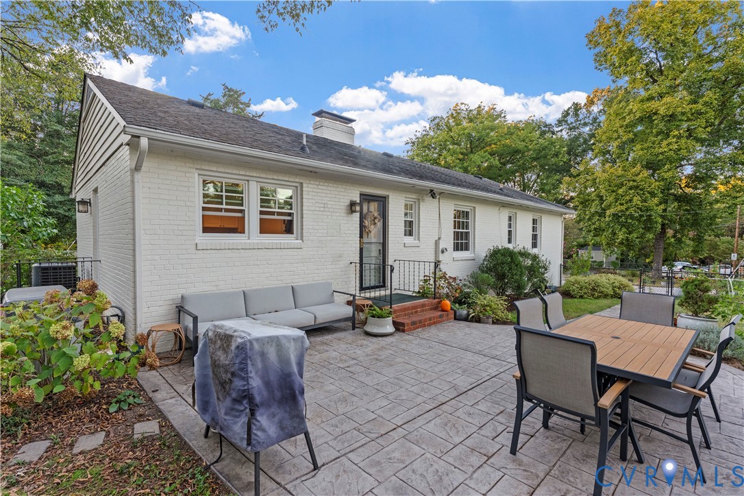 Painted brick exterior featuring a stamped concrete patio, red brick steps, metal railings, and a chimney