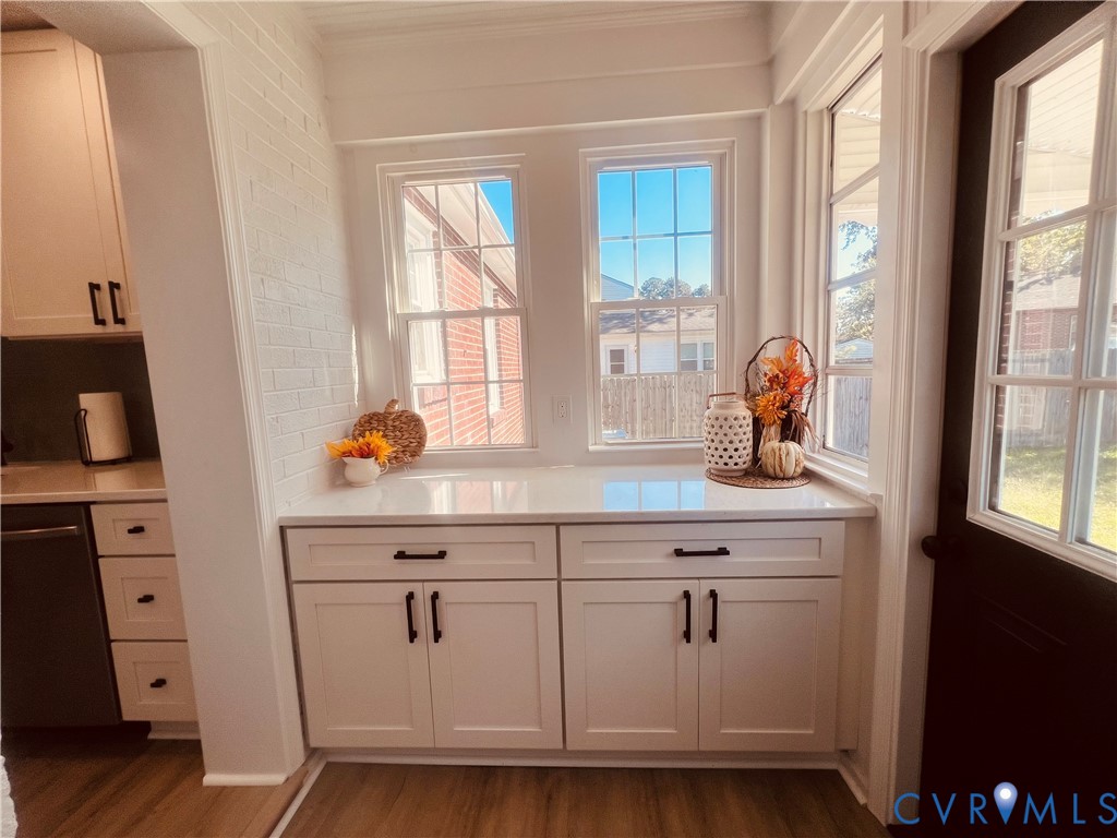 Built-in white cabinetry featuring shaker-style doors, matte black hardware, and solid surface countertops, accented by painted brick walls and multi-pane windows