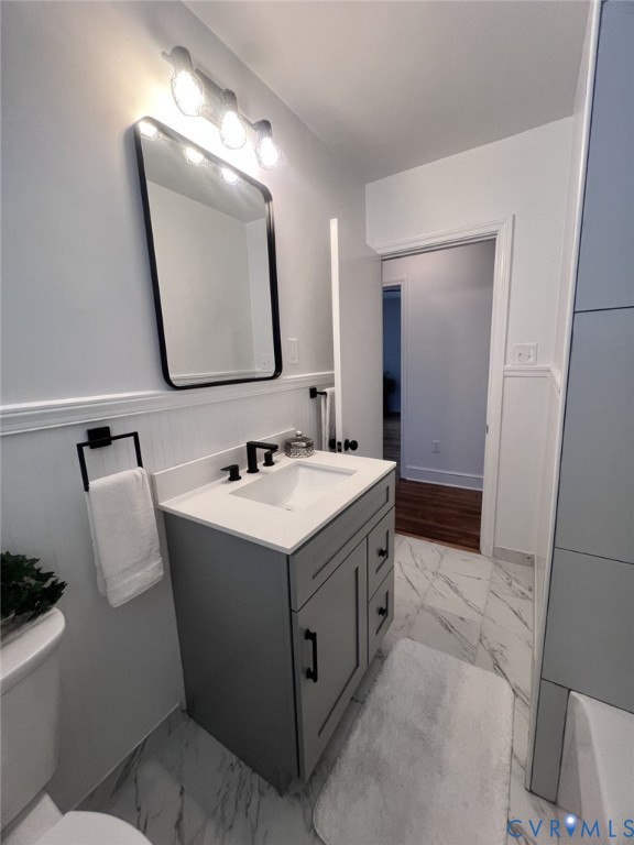 Modern vanity featuring a stone-composite countertop, rectangular undermount sink, matte black hardware, vertical wainscoting, and marble-finish tile flooring