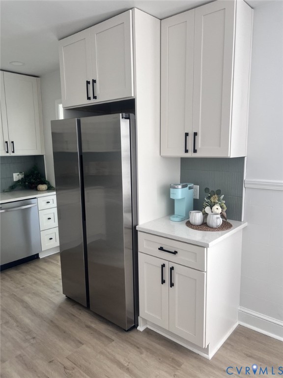 White shaker-style cabinetry with matte black hardware, stainless steel refrigerator, light-toned quartz countertops, and vertical tiled backsplash