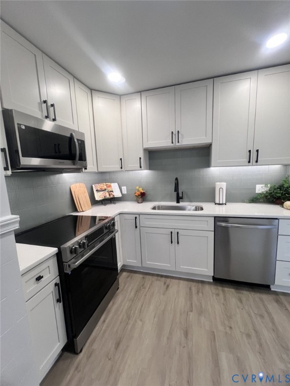 Kitchen featuring white cabinetry with matte black hardware, light-toned stone-finish countertops, tiled backsplash, stainless steel appliances, and wood-finish flooring