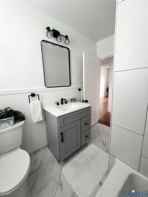 Grey vanity with a white countertop and undermount sink, marble-patterned tile flooring, rectangular mirror with a black frame, and matte black plumbing fixtures