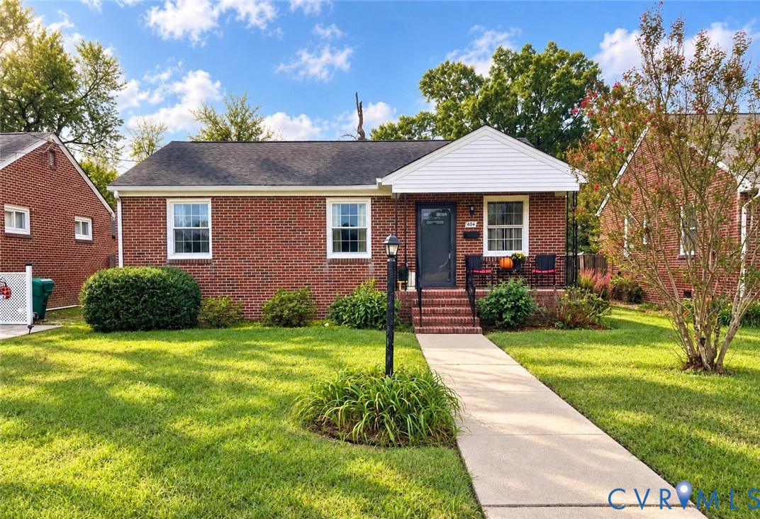 Classic brick exterior featuring a covered front porch, a central entryway, a concrete walkway, and a landscaped front lawn Classic brick exterior featuring a covered front porch, a central entryway, a concrete walkway, and a landscaped front lawn