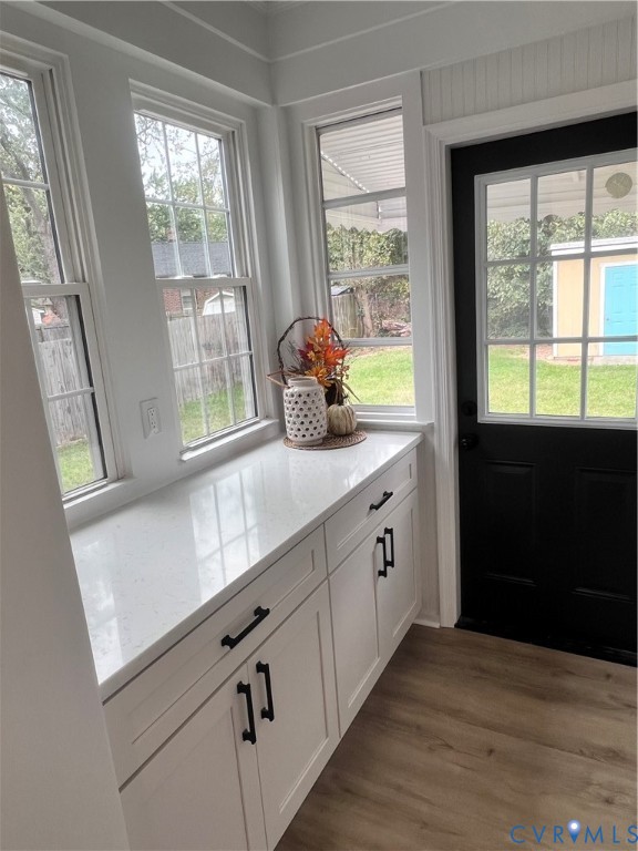 Custom cabinetry featuring matte black hardware, stone-surface countertop, wood-finish flooring, multi-pane windows, and a multi-pane glass door