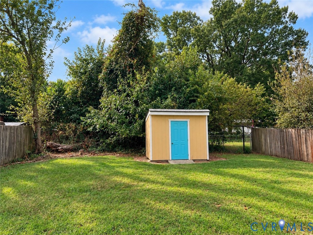 Backyard featuring a standalone storage structure with a shed-style roof, wood fencing, and mature trees