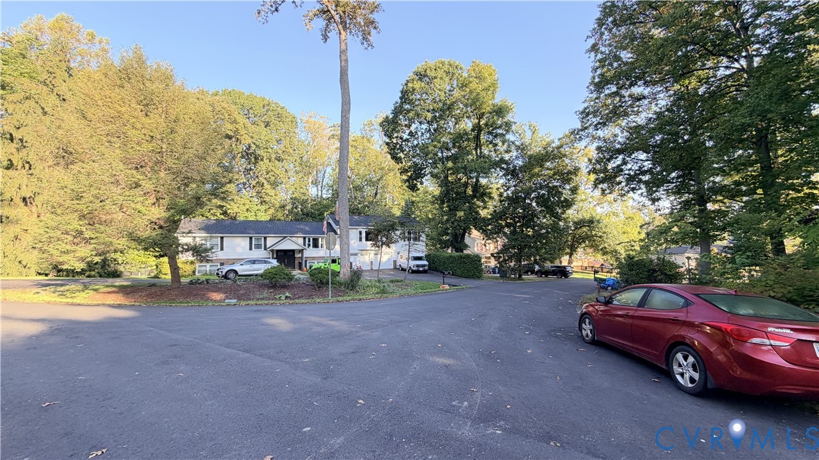 Two-story residence featuring light-colored siding, a multi-car garage, and mature trees on a lot with an expansive asphalt driveway Two-story residence featuring light-colored siding, a multi-car garage, and mature trees on a lot with an expansive asphalt driveway