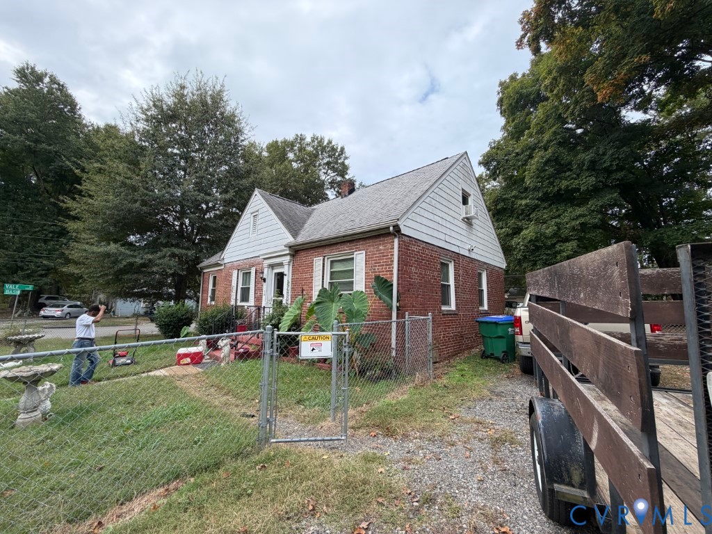 Brick exterior featuring a gabled roofline, light-colored siding accents, and a chain-link fenced perimeter