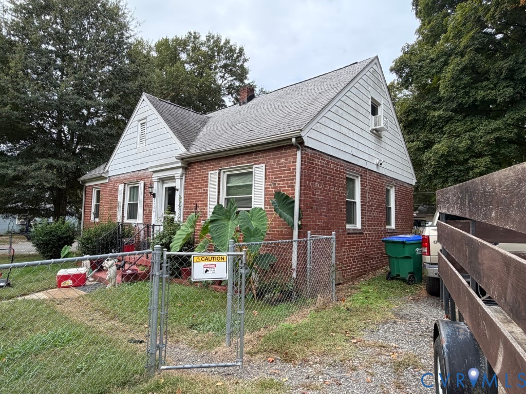 Single-story brick exterior featuring a gable roofline, white horizontal siding, window shutters, and a gated chain-link fence