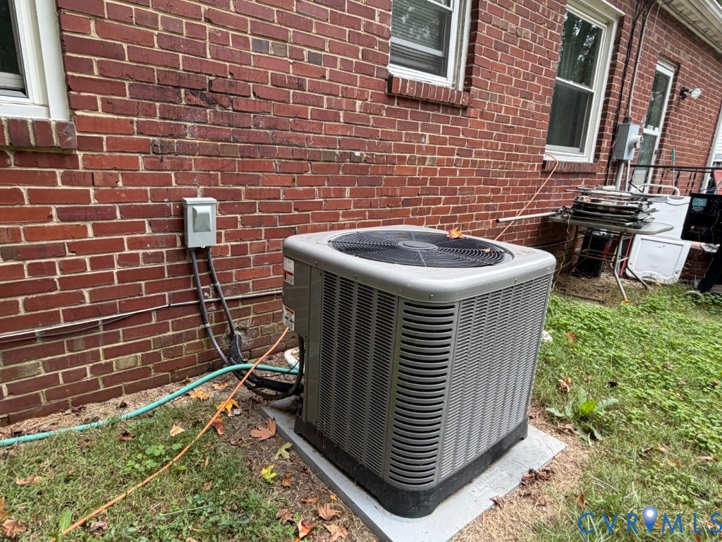Exterior central air conditioning unit positioned on a concrete slab against a red brick facade with double-hung windows
