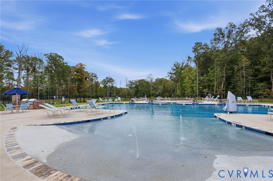 Outdoor swimming pool featuring a zero-entry design with integrated water jets, stone-finish masonry, concrete decking, and a brick-encased built-in grilling station