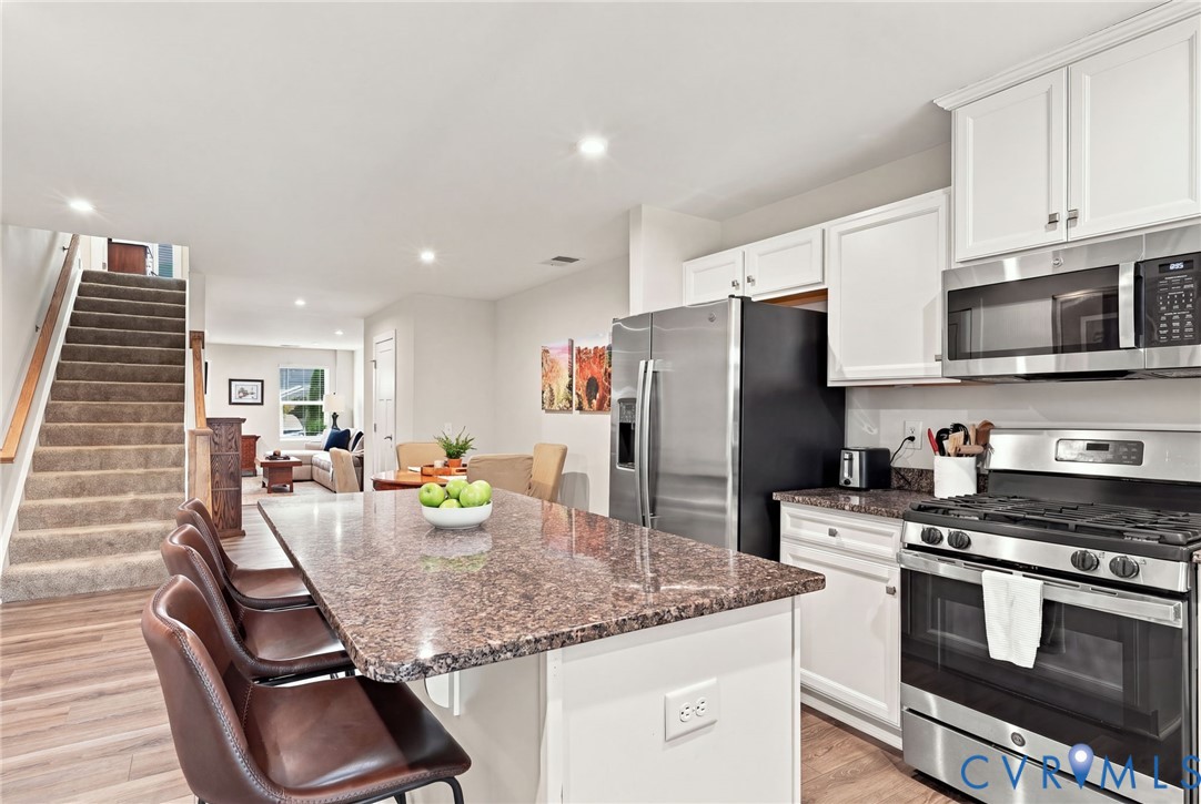 Kitchen featuring white shaker-style cabinetry, stone-surface countertops, an oversized center island, and stainless steel appliances including a gas range and microwave