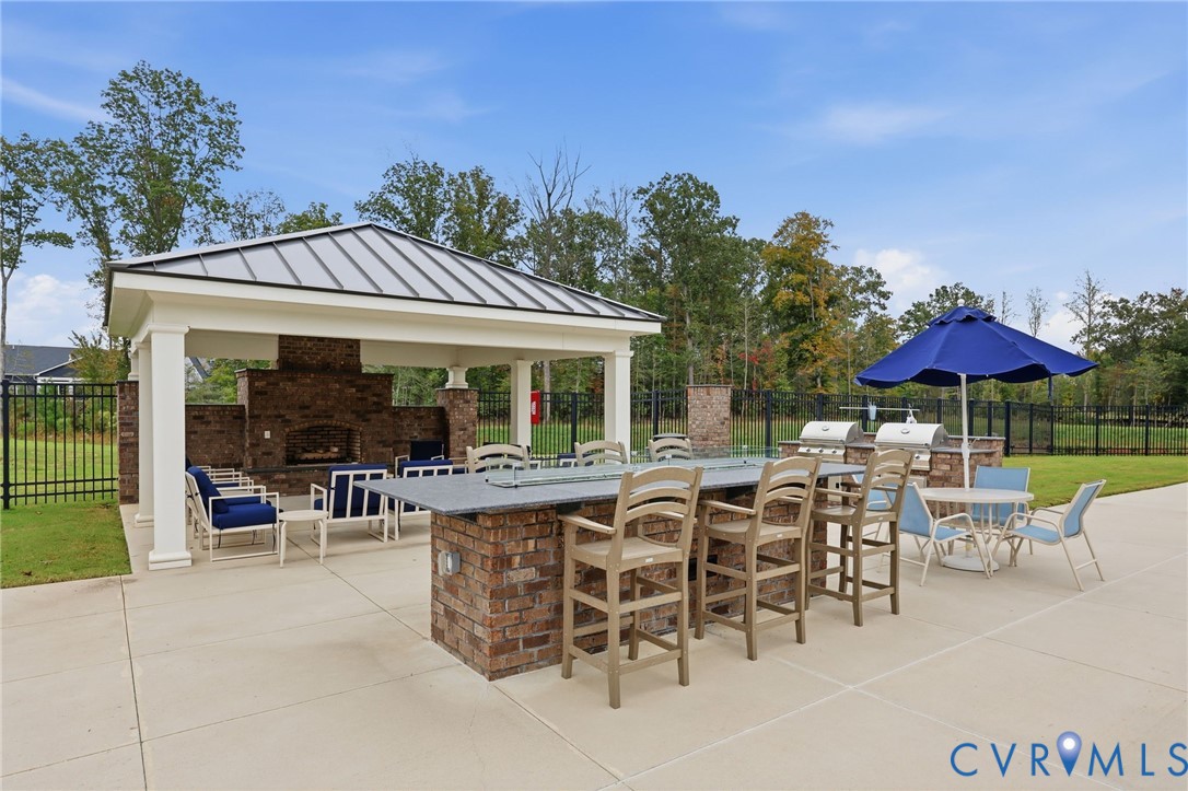 Outdoor pavilion featuring a metal roof, a brick masonry fireplace, a stone-topped island with an integrated fire feature, and a built-in outdoor kitchen