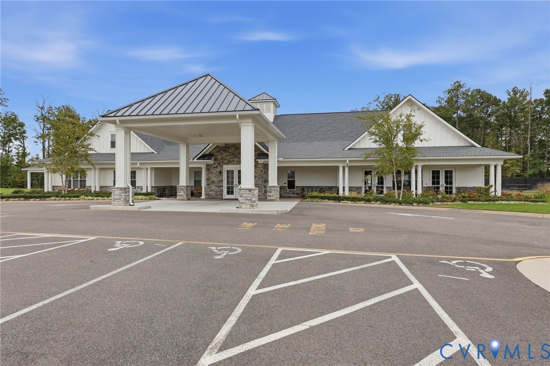 Exterior facade featuring a metal-roof porte-cochre, stacked stone accents, horizontal siding, and multiple glass-paneled double door entrances