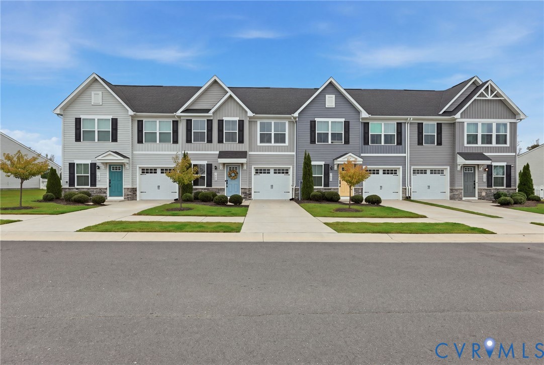 Multi-unit townhouse exterior featuring mixed siding, stone veneer accents, individual garages, and concrete driveways