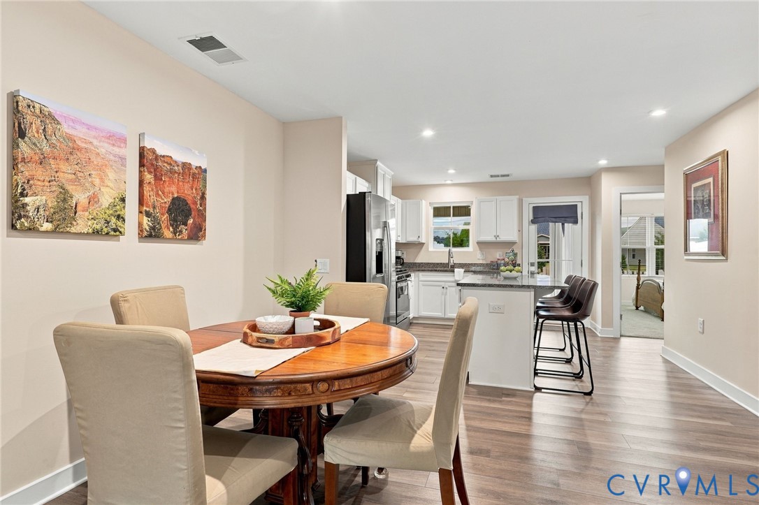 Kitchen featuring white cabinetry, stone countertops, a center island with seating, stainless steel appliances, and wood-finish flooring