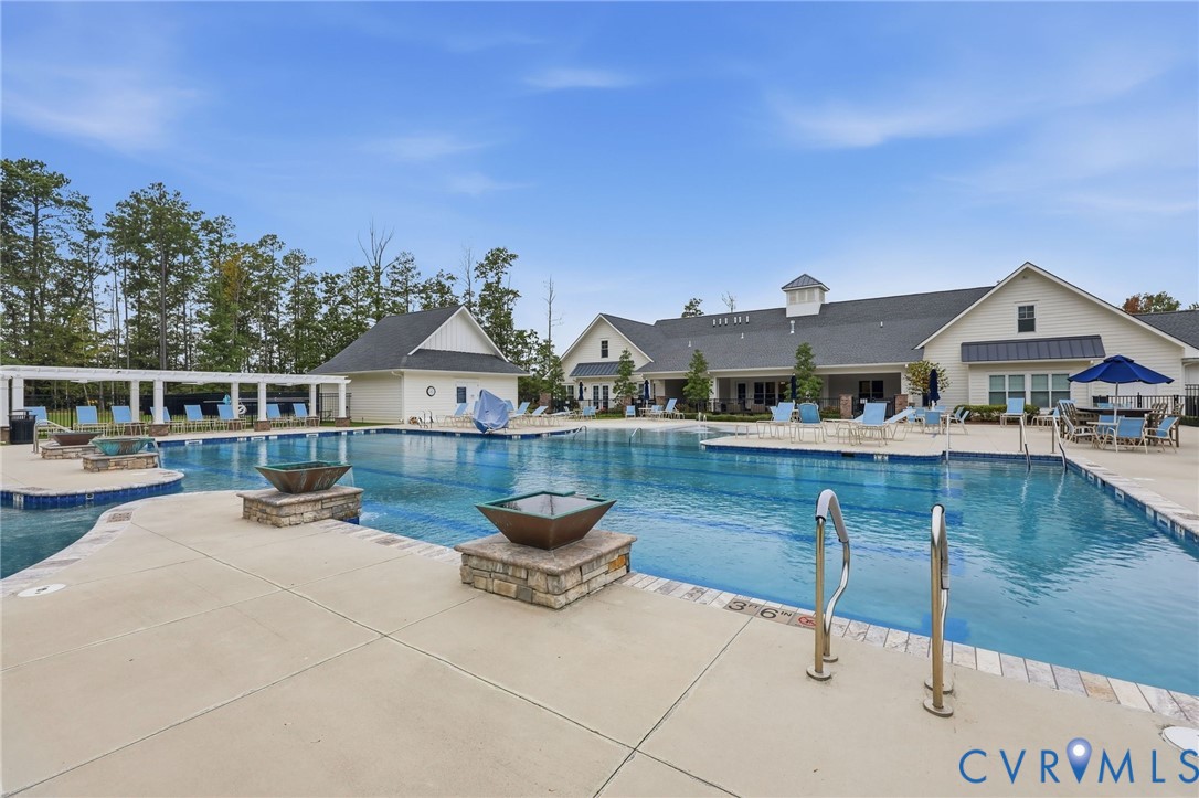 Swimming pool featuring stone-clad fire features, concrete decking, and a pergola-covered patio area