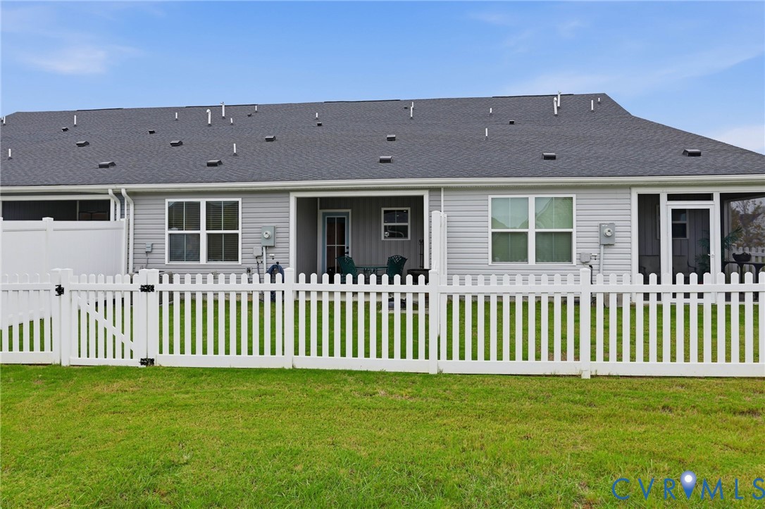 Rear exterior featuring vinyl siding, a gabled asphalt shingle roof, white vinyl picket fencing, and a covered patio