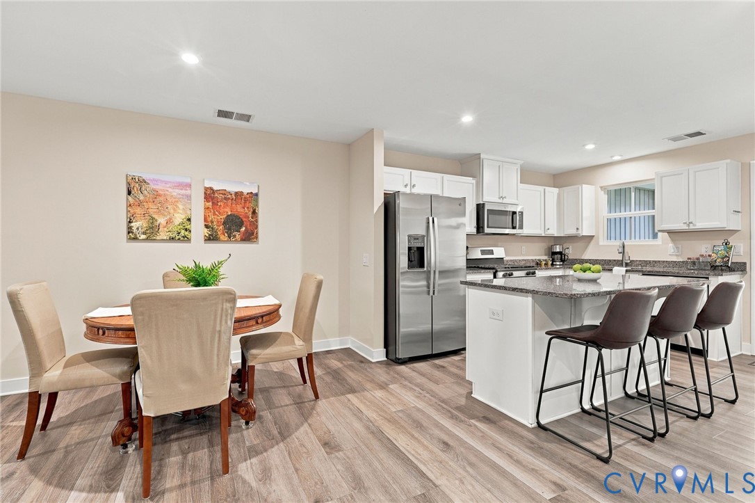 Kitchen featuring white shaker-style cabinetry, an expansive central island with stone-finish countertop, recessed lighting, and wood-finish flooring