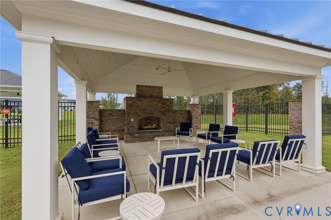 Covered outdoor pavilion featuring a concrete patio, a brick-surround fireplace, structural columns, and a ceiling-mounted fan