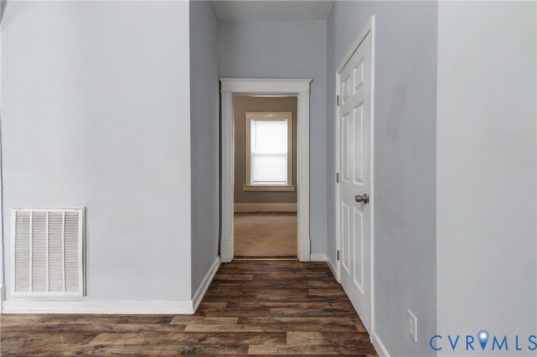 Wood-finish flooring, interior doorway with white-painted trim, and a six-panel door with a metallic knob