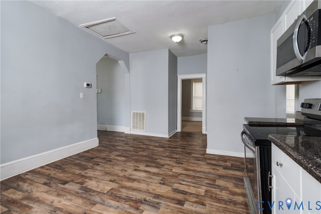 Kitchen featuring white cabinetry, dark countertops, built-in stainless steel microwave, and wood-finish flooring
