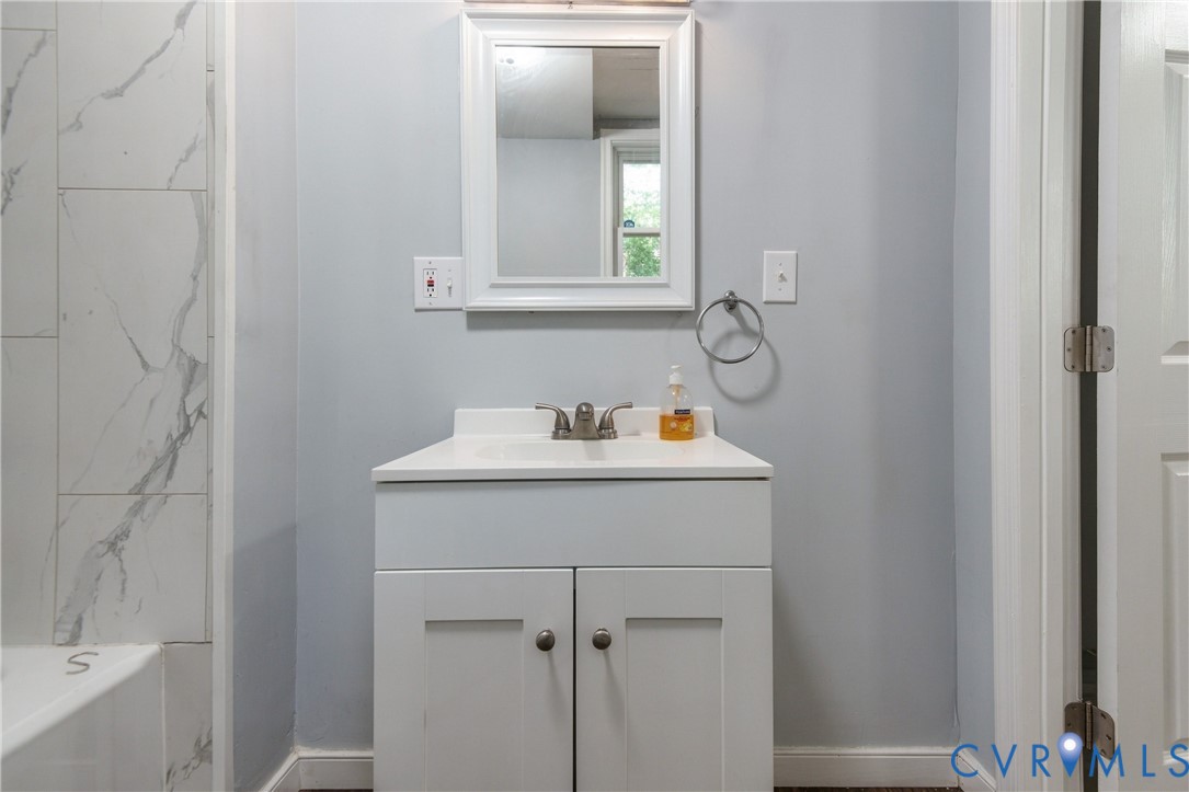 White vanity cabinet with an integrated rectangular basin, chrome dual-handle faucet, framed wall mirror, and floor-to-ceiling tile shower surround