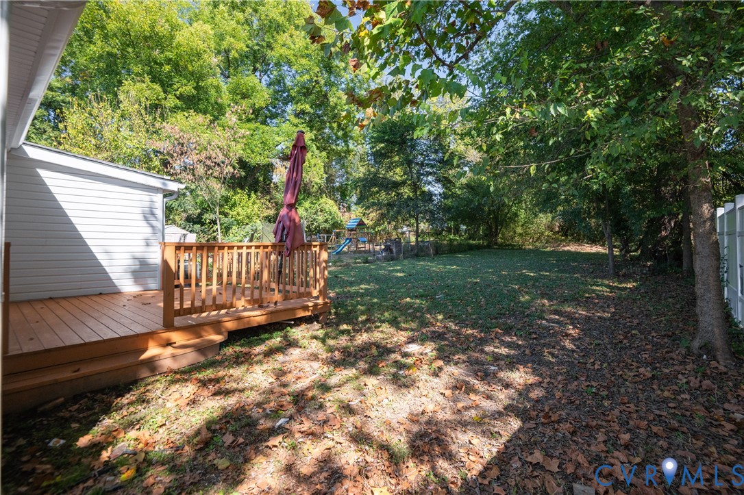 Rear exterior featuring a raised wood deck with balustrades, white vinyl siding, and a fenced backyard with mature trees