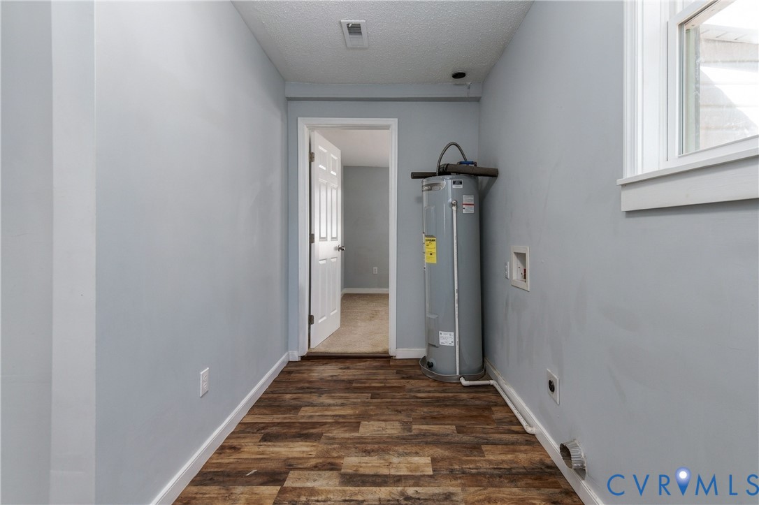 Utility area featuring wood-finish flooring, a vertical water heater, a window with white trim, and a six-panel interior door