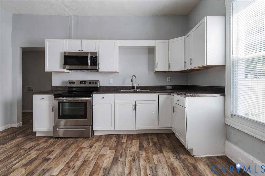 Kitchen featuring white shaker-style cabinetry, dark stone-finish countertops, stainless steel appliances, wood-finish flooring, and a single-basin sink with a gooseneck faucet