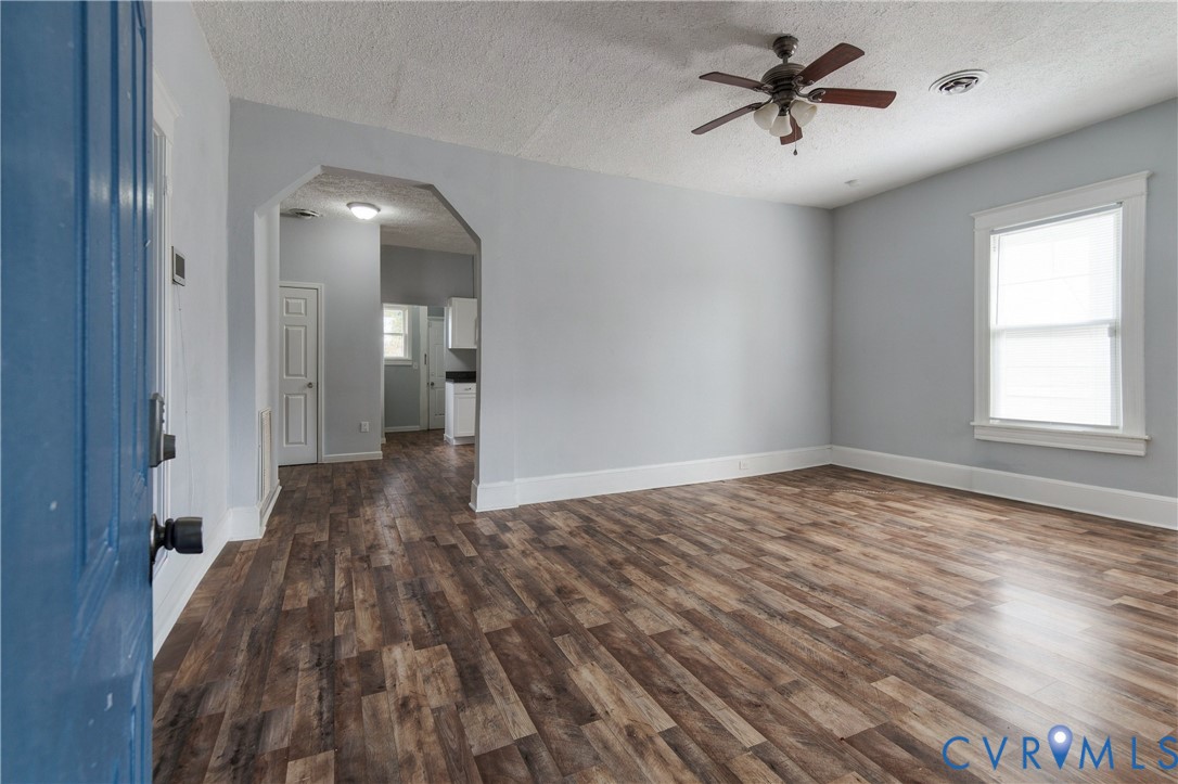 Living area featuring wood-finish flooring, a neutral color palette, a ceiling fan with integrated lighting, and a multi-pane window with custom trim