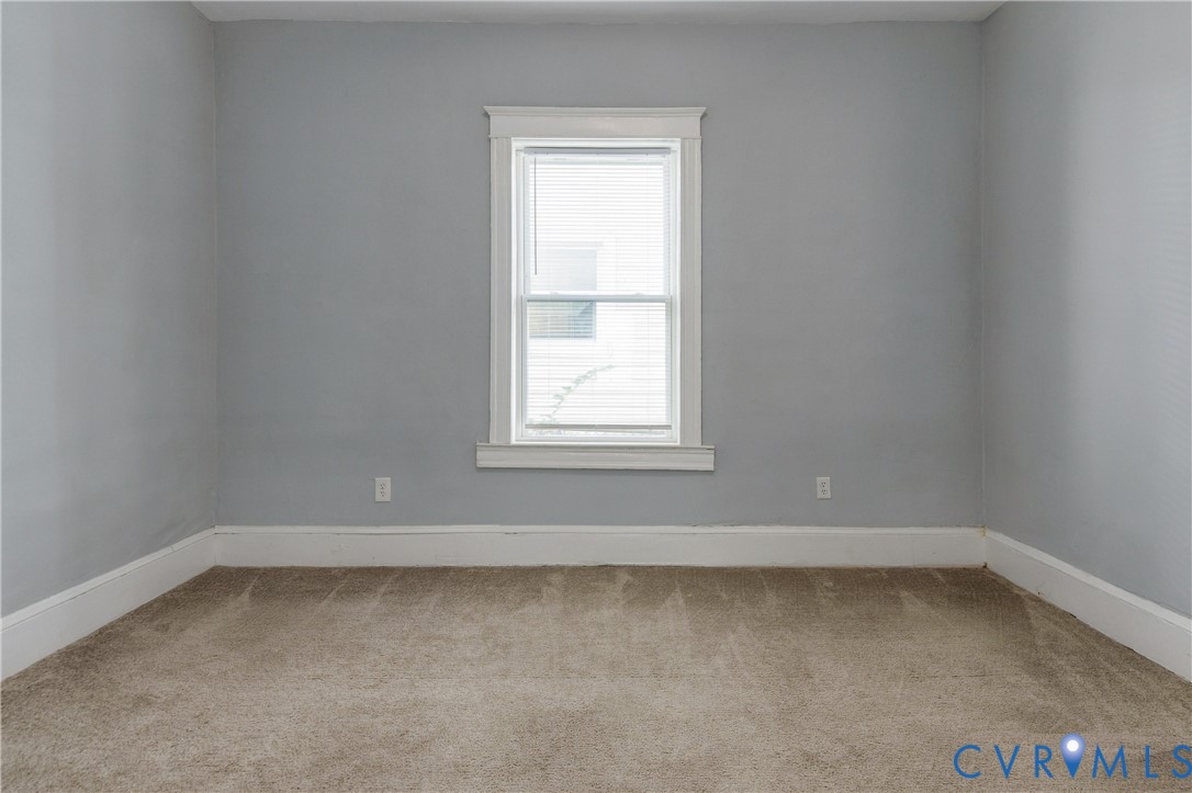 Neutral-toned wall paint, neutral carpeting, and a centrally positioned window featuring white trim and molding