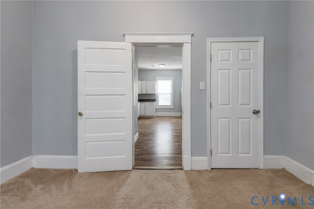 Interior space featuring neutral wall paint, white-painted wood trim, a four-panel door, a six-panel door, and wood-finish flooring visible through the doorway