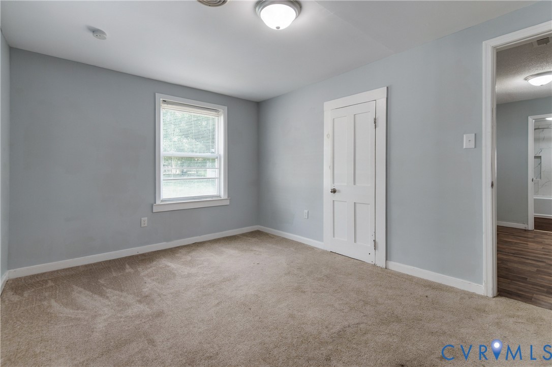 Neutral-toned interior room featuring wall-to-wall carpeting, a single-hung window, a multi-panel interior door, and a flush-mount ceiling light fixture