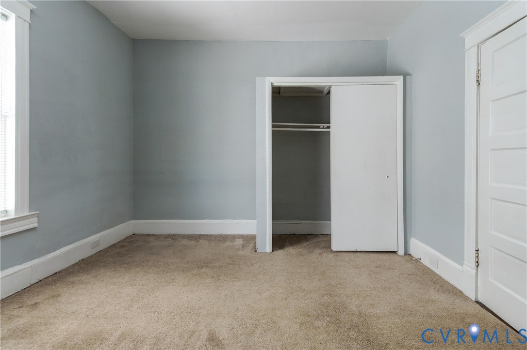 Interior room featuring neutral-toned carpeting, a built-in closet with sliding doors, and traditional multi-panel door and window casings