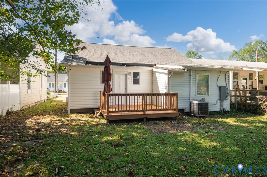 Rear exterior featuring white vinyl siding, a wooden deck, and a grass-covered backyard