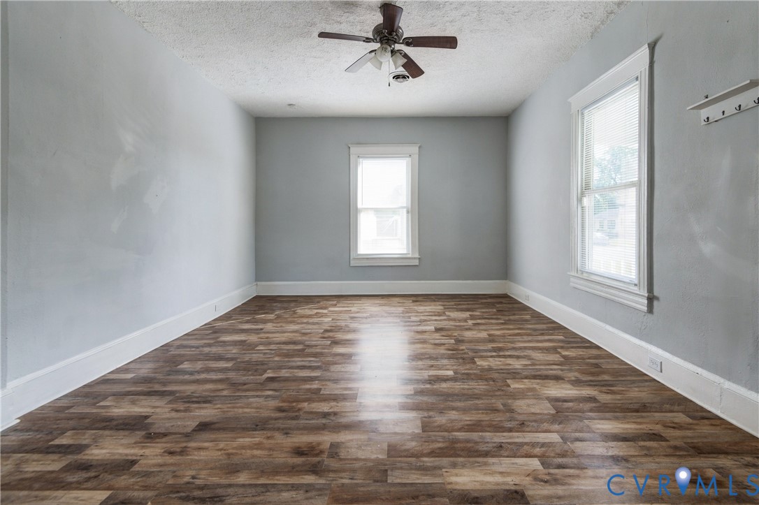 Interior room featuring wood-finish flooring, neutral wall paint, two windows with white trim, and a ceiling-mounted fan